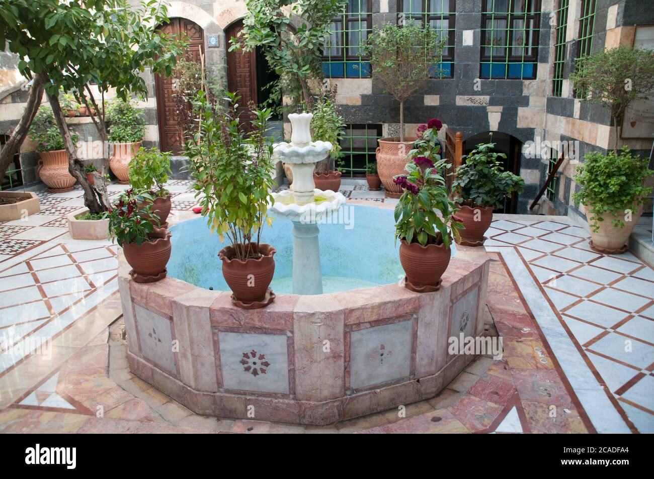 A decagonal water fountain and potted plants in a traditional Syrian