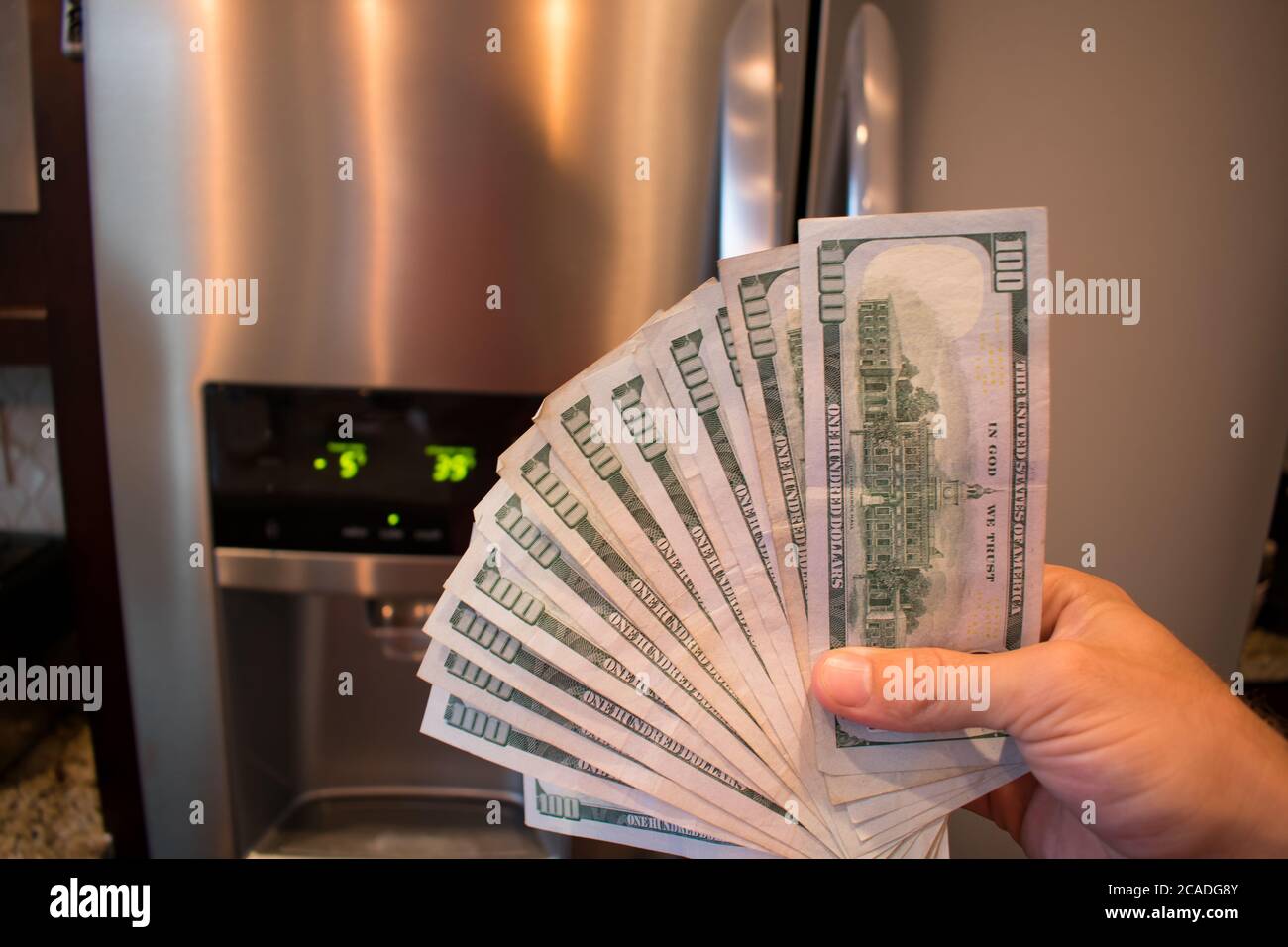 Fanned 100 dollar bills In front of a broken refridgerator Stock Photo