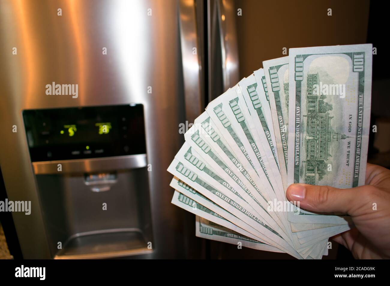 Fanned 100 dollar bills In front of a broken refrigerator Stock Photo