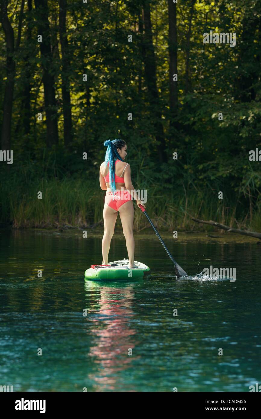 Woman with blue braids standing on an inflatable boat on river and holding a paddle. Mid shot Stock Photo
