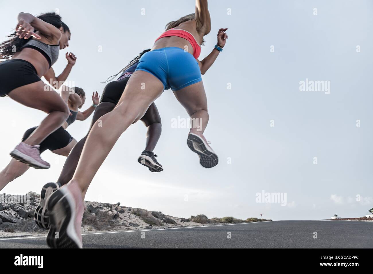 From below energetic multiethnic sportswomen running fast on road during training in evening Stock Photo