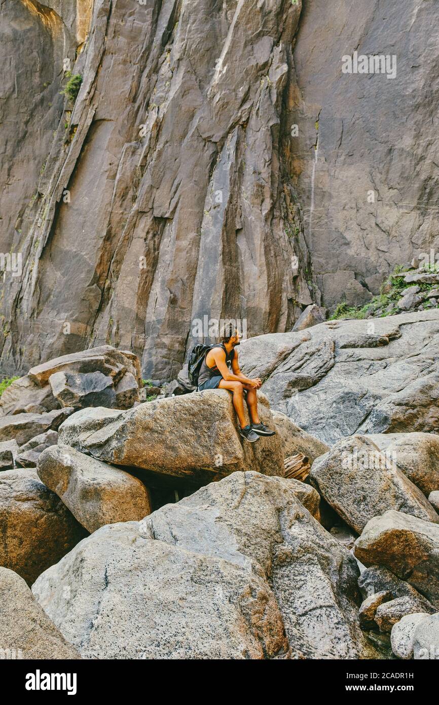 Young man resting on boulder, observing Yosemite Falls. Stock Photo
