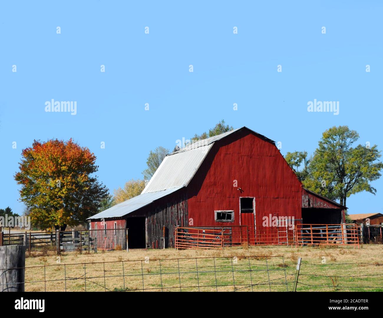 Arkansas farm site has a red tin covered barn.  Tin roof and no loft door.  Sky is blue. Stock Photo