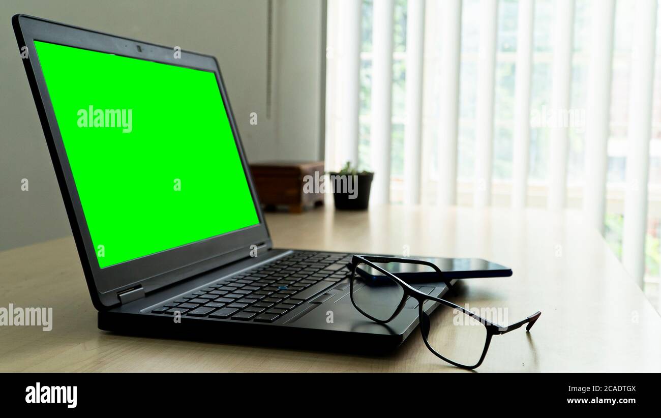 laptop on wooden desk with green screen glasses and smartphone with blur background Stock Photo