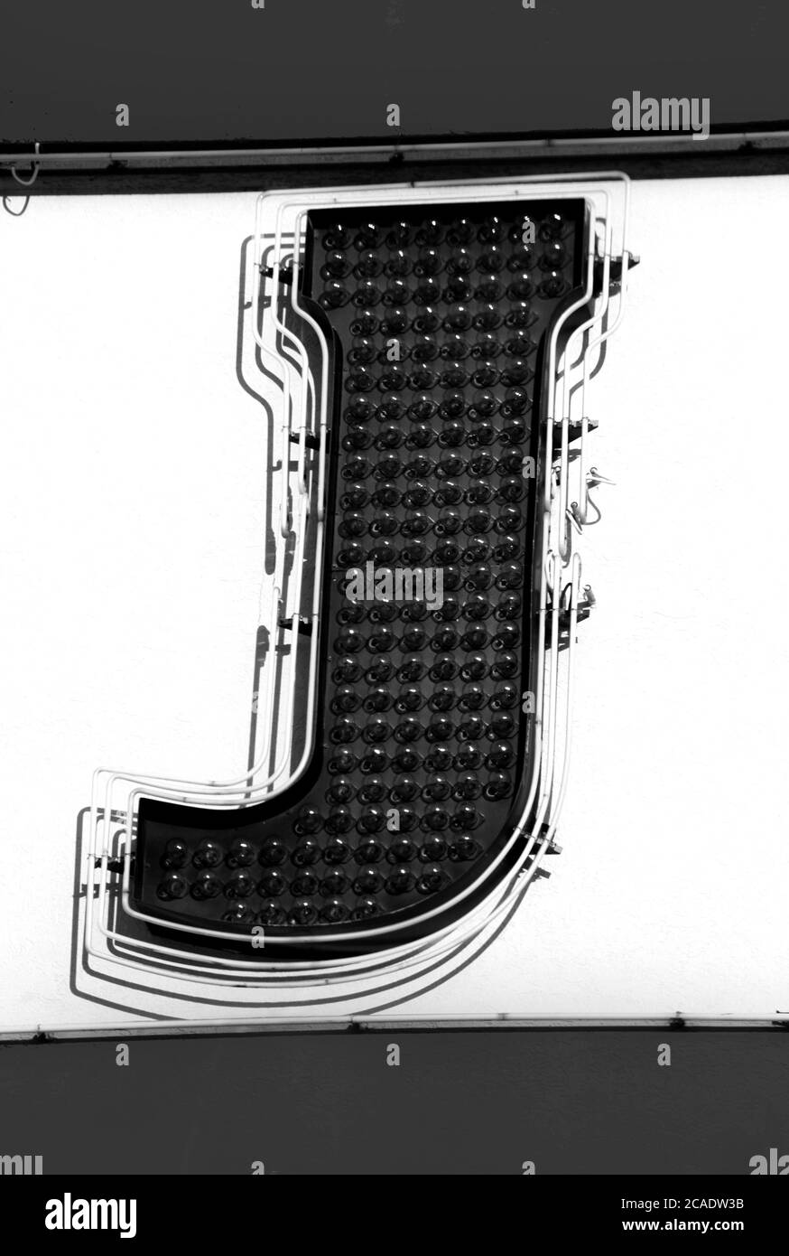 The letter J is formed by clear light bulbs.  Neon lights outline the letter.  Black and white image. Stock Photo