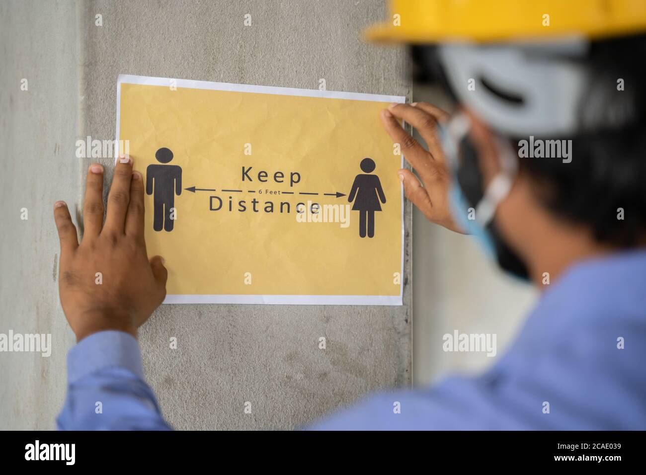 worker pasting Keep 6 feet distance on wall at work place or construction site due to coronavirus or covid-19 pandemic - concept of safety measures Stock Photo