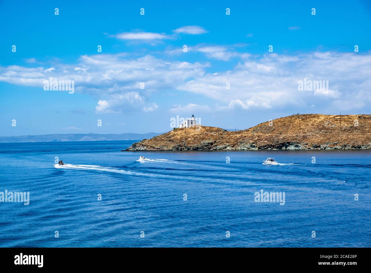 Inflatable speed boats cruising in mediterranean sea.  Lighthouse on a cape, blue cloudy sky and sea water background, sunny day. Greece, Kea Tzia isl Stock Photo