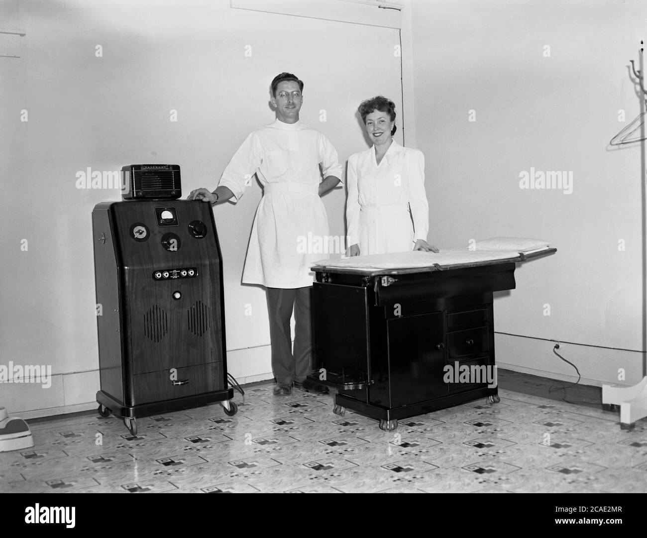 cicra, 1940s, historical, in a large open surgery, a professional male chiropodist wearing a white medical top standing with his female client. Stock Photo