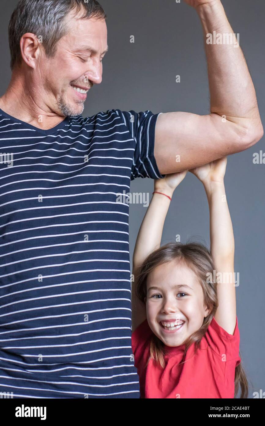 A cheerful girl hangs on her father's strong arm. Father's day Stock Photo