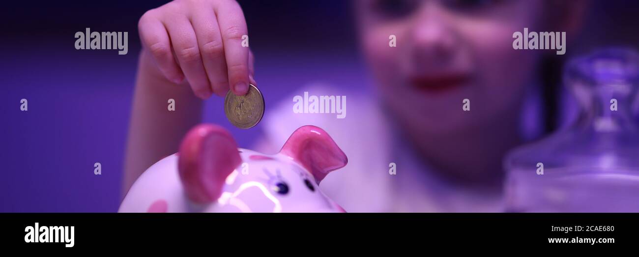 Little girl puts coin in piggy bank on table Stock Photo - Alamy