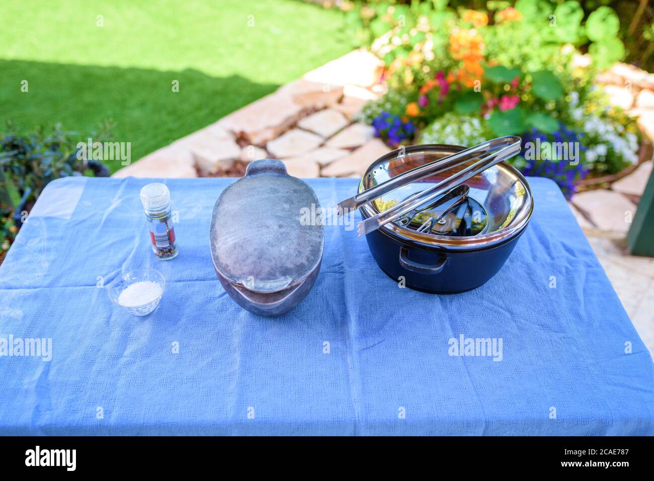 Preparing for a barbecue outside in the Summer Garden. Pots, bbq tongs, salt, spices on a table with a blue tablecloth.Retro style. Stock Photo
