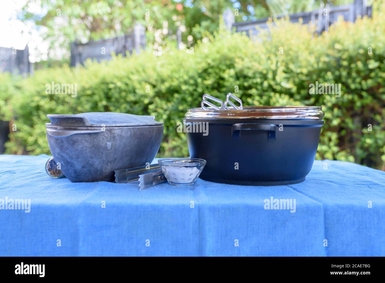 Preparing for a barbecue outside in the Summer Garden. Pots, bbq tongs, salt, spices on a table with a blue tablecloth.Retro style. Stock Photo