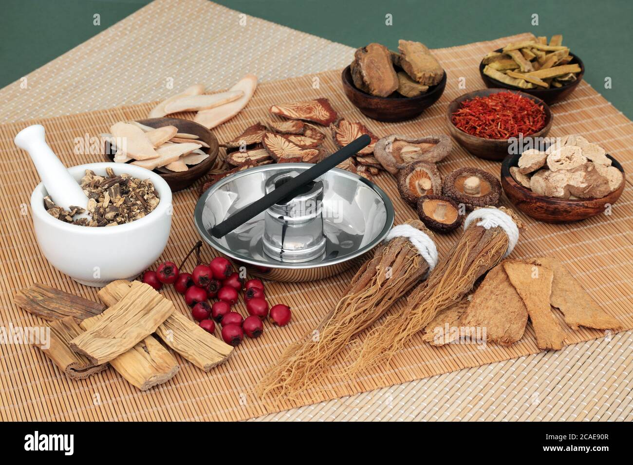 Chinese herbal medicine selection and moxa stick used in moxibustion therapy with mortar and pestle on bamboo mat and mottled green background. Stock Photo