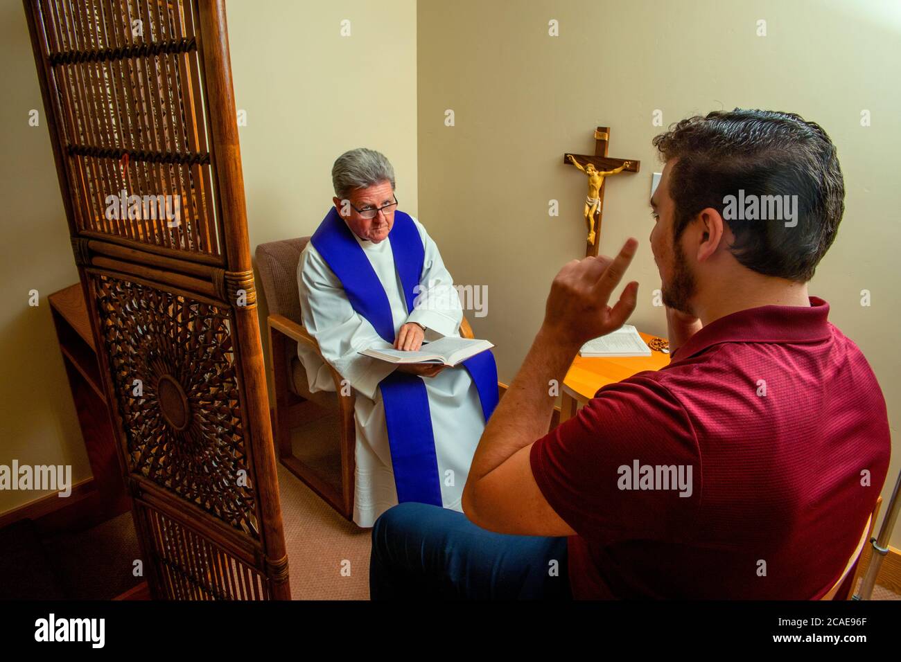 A robed monsignor conducts face to face confession with a young adult penitent at a Southern California Catholic church. Stock Photo