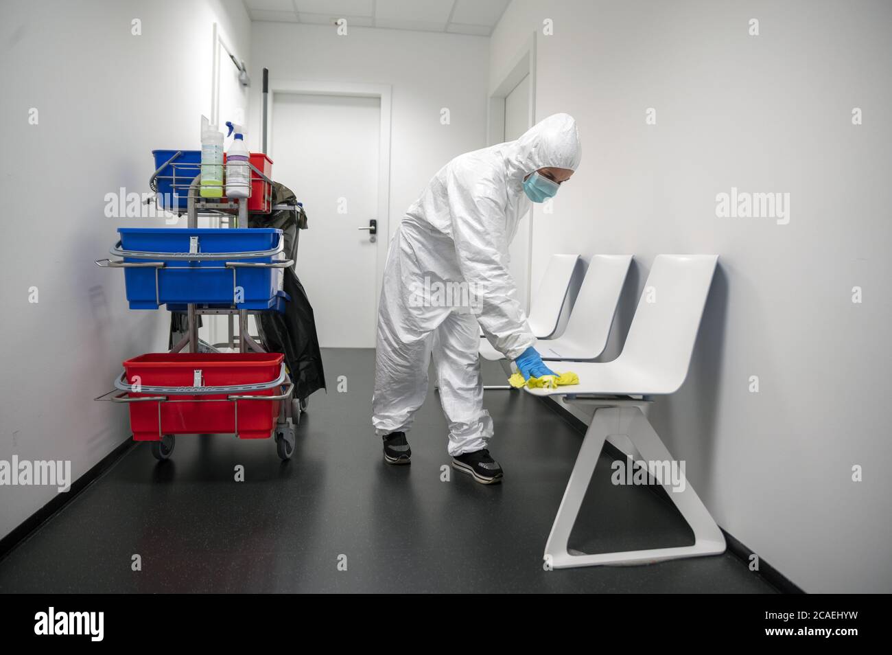 Alert Corona Virus or Covid-19. Cleaner with full protective suit, masks and gloves cleans, disinfects and sanitizes the waiting roorm and chairs. Stock Photo
