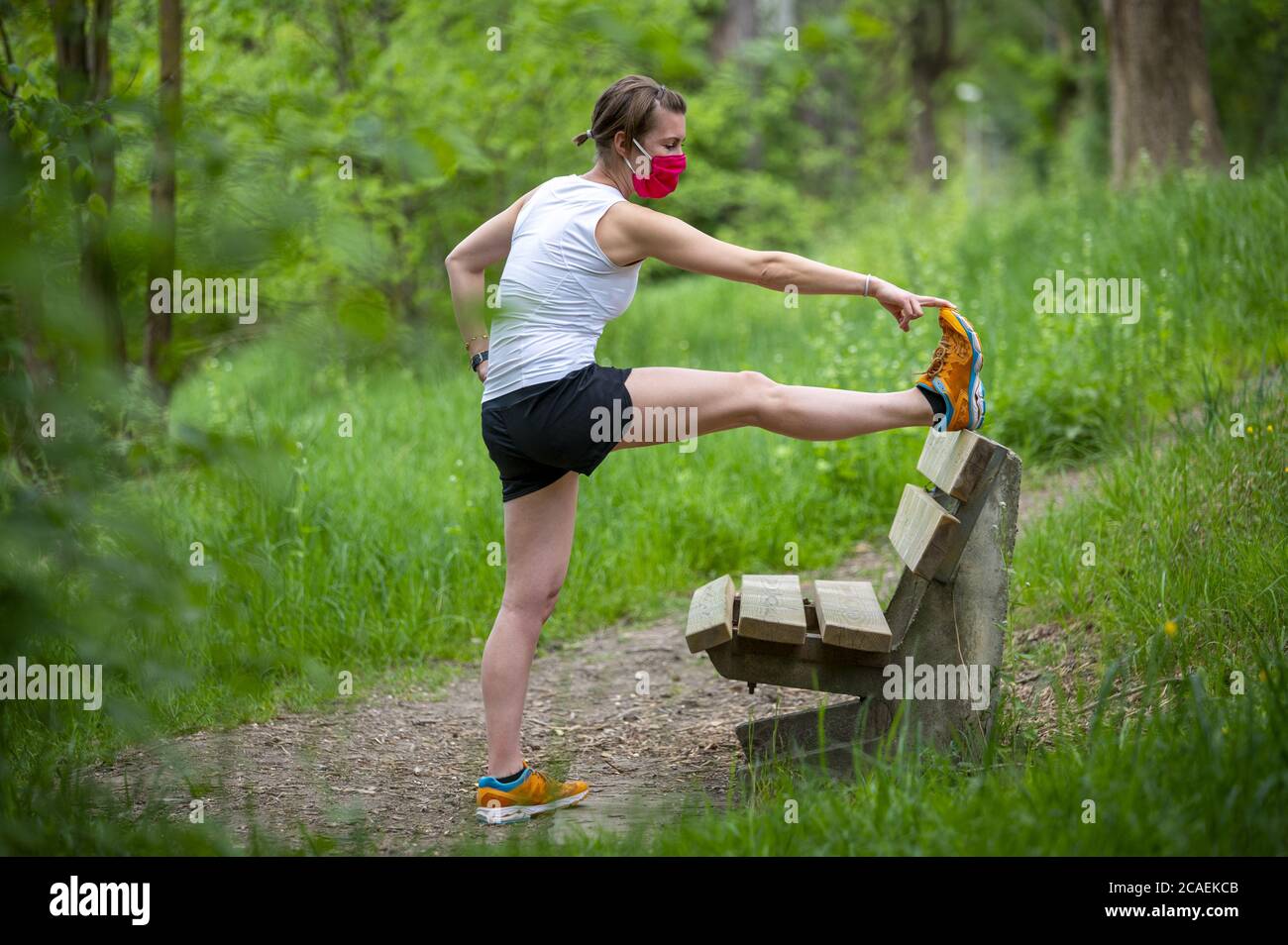 Stay in fit during Coronavirus. A sportive woman is jogging outdoor, she have protective mask on face. Running in the days of the Covid-19. Stock Photo