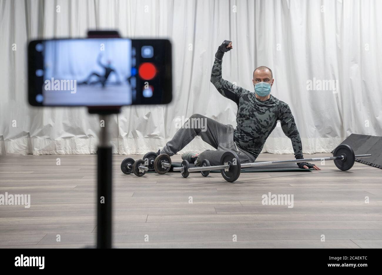Man with gym dumbbell and balance. Workout exercises live on smartphone for sportive follower on the social media. Coronavirus or Covid-19 quarantine. Stock Photo