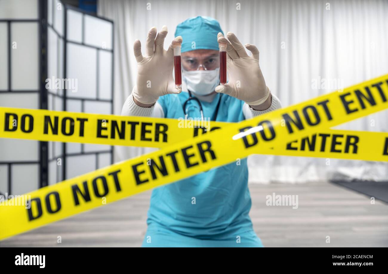 Doctor with glasses, gloves and mask holding test tubes with blood for 2019-nCoV analyzing. Corona virus or Covid-19 blood test. Do not enter tape. Stock Photo