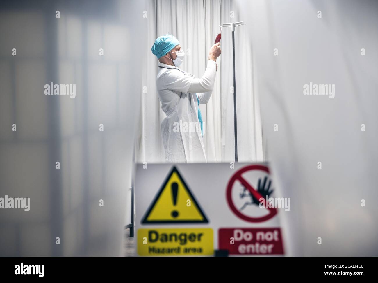 Doctor with protective mask and gloves checks the blood iv before administering it to a patient infected with Corona Virus. Yellow tape, Do Not Enter. Stock Photo