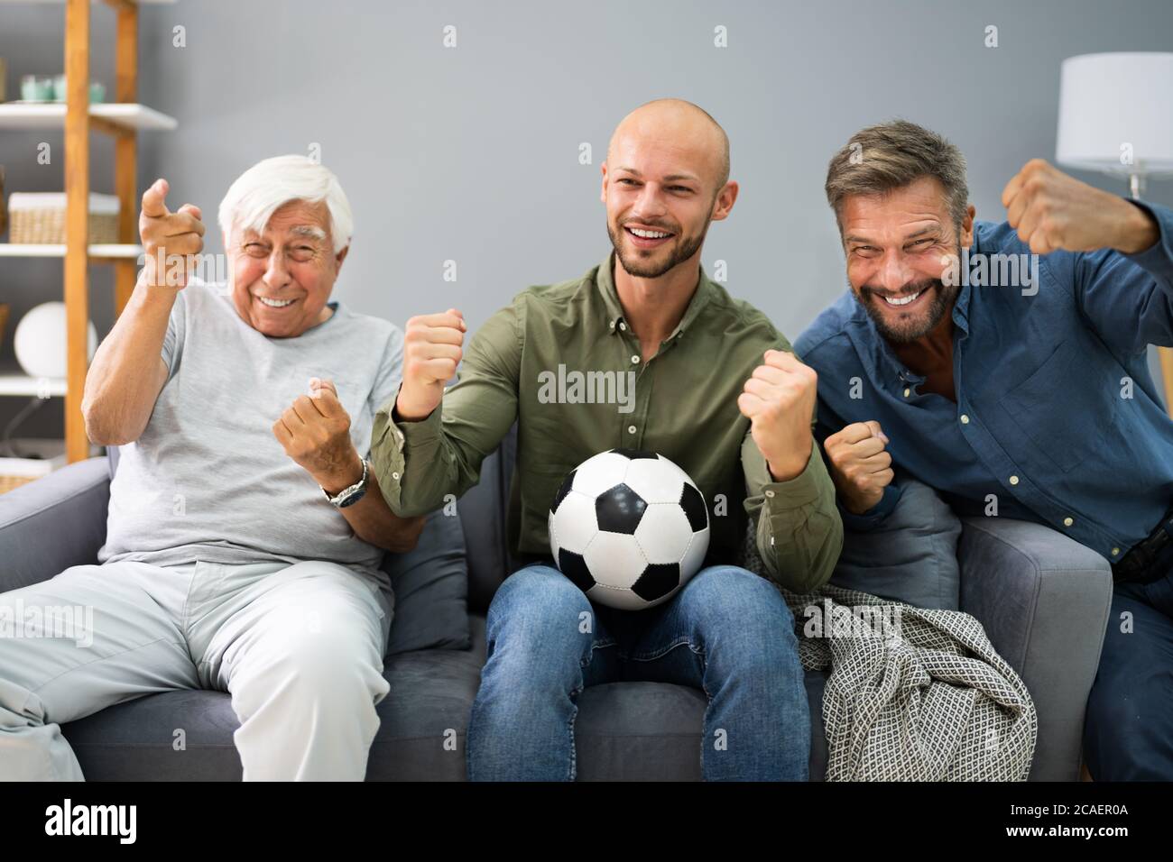 Three Generation Sport Fans Watching Football On TV Stock Photo
