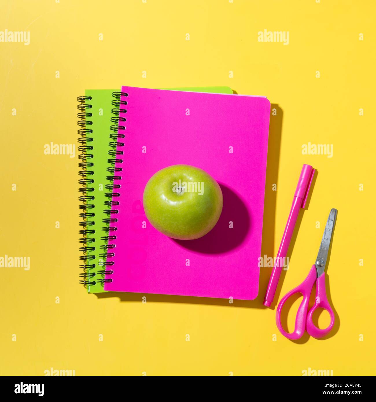 School bright supplies, notebooks, scissors, apple on yellow background. Top view, flat lay. Stock Photo