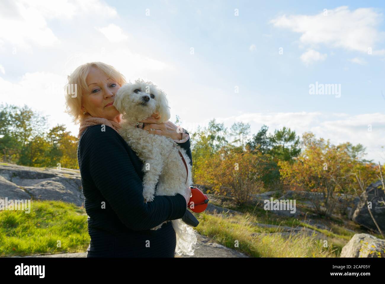 Senior woman holding dog and standing on boulder in the mountains Stock Photo