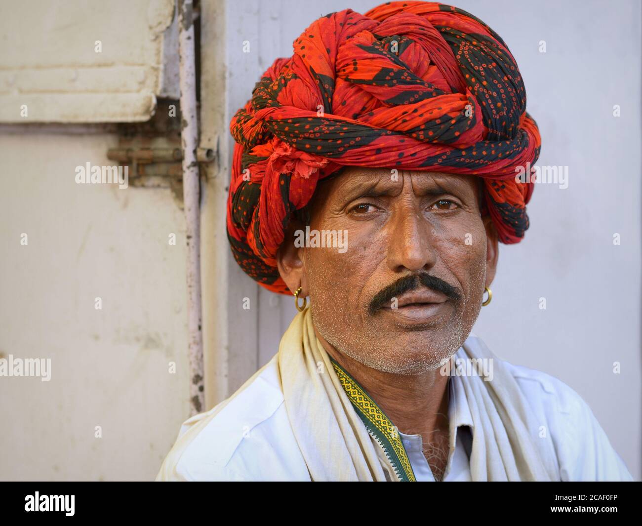 Indian Rajasthani man with black moustache and stylish red-and-black turban (pagari, pagdi) looks at the camera. Stock Photo