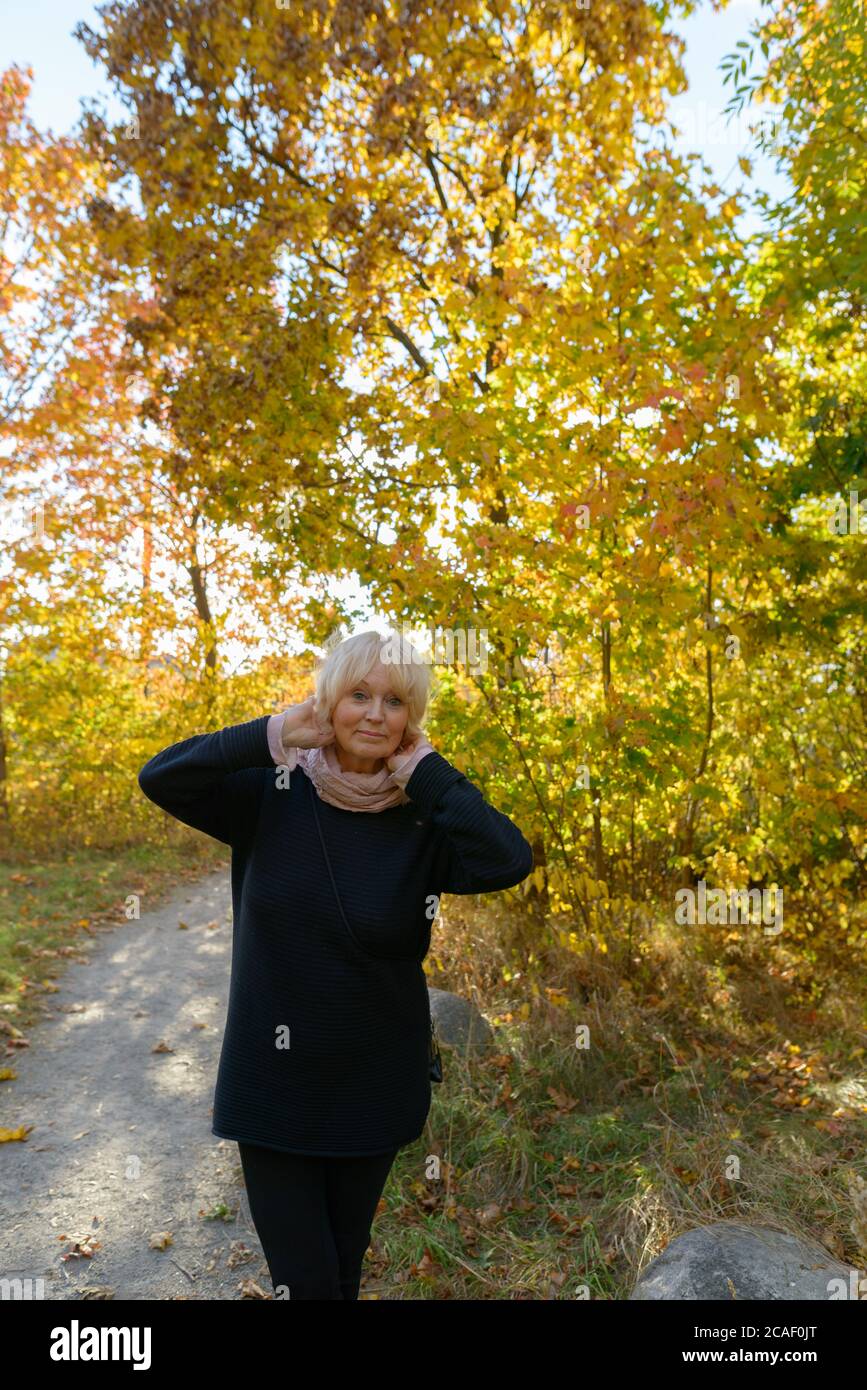 Senior woman posing on small pathway in the forest with young autumn trees Stock Photo