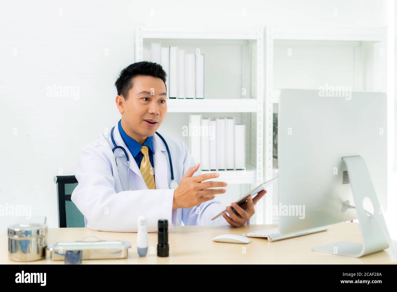 Asian man doctor wears white coat and headset speaking videoconferencing on laptop computer using online video call consultation app. Remote medical h Stock Photo