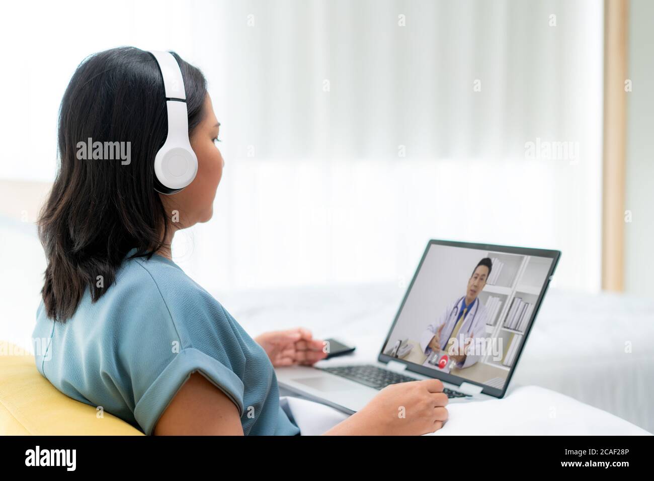 Back view of Asian woman making video call with her doctor with her feeling sick on laptop in bedroom for online healthcare digital technology service Stock Photo