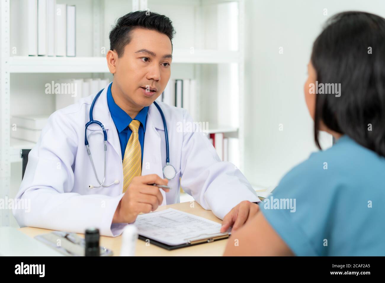 Asian man doctor and woman patient are discussing consultation about symptom problem diagnosis of disease talk to the patient about medication and tre Stock Photo