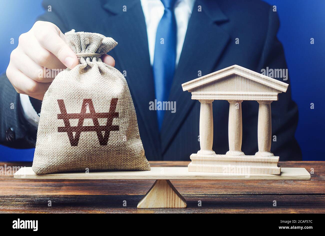 Businessman puts a south korean won money bag on scales opposite to government state building. Payment of taxes and fees. Financing Social programs. L Stock Photo