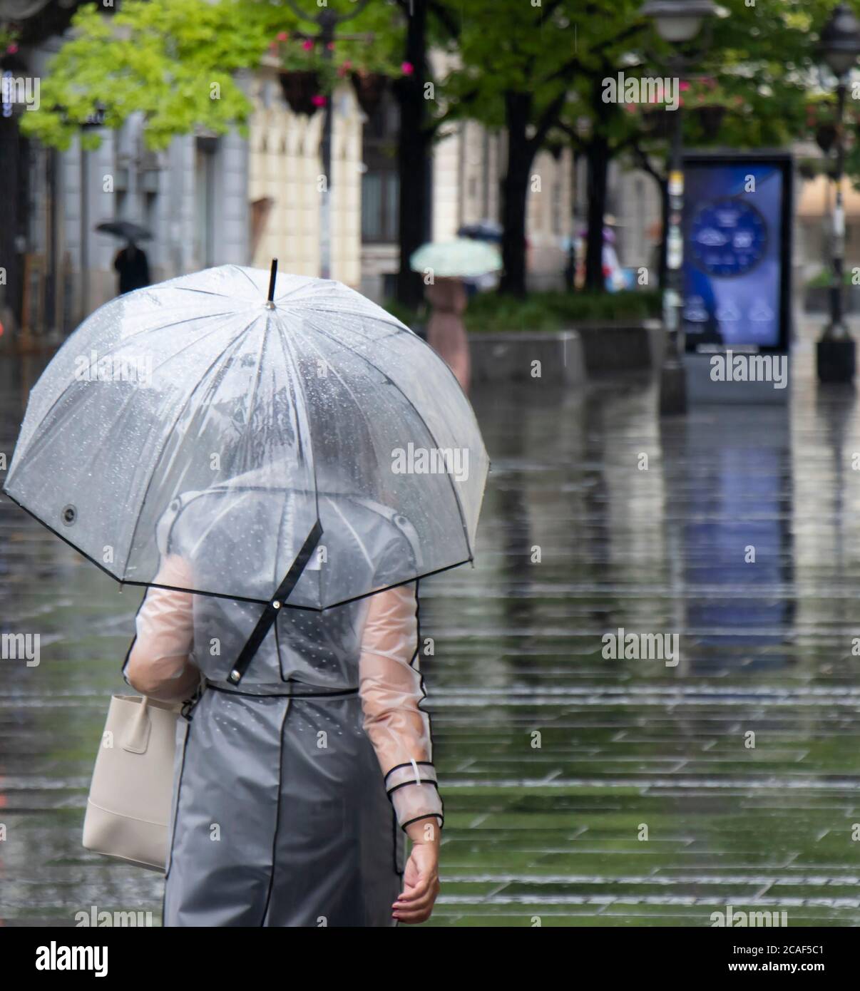 Woman in transparent raincoat walking under umbrella on a rainy summer day in the city of Belgrade, Serbia Stock Photo