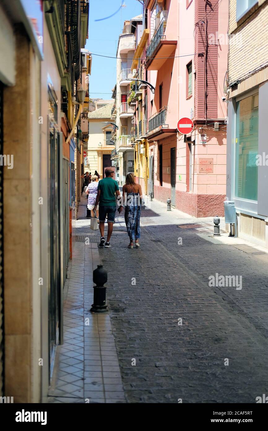 Middle aged tourist couple holding hands while walking down a quiet narrow street in Granada, Spain. Stock Photo
