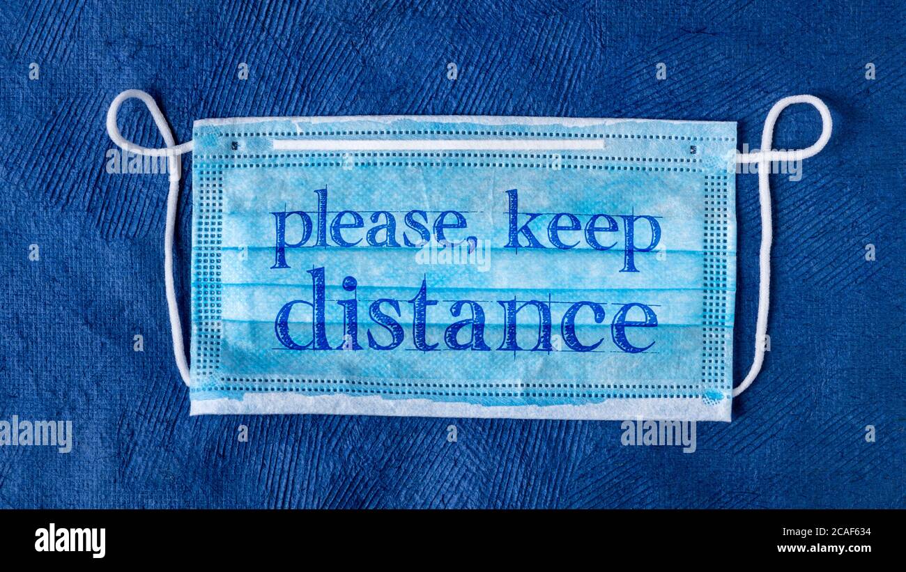 please, keep distance - text on a disposable mask against blue textured paper, social distancing during the coronavirus covid-19 pandemic concept Stock Photo