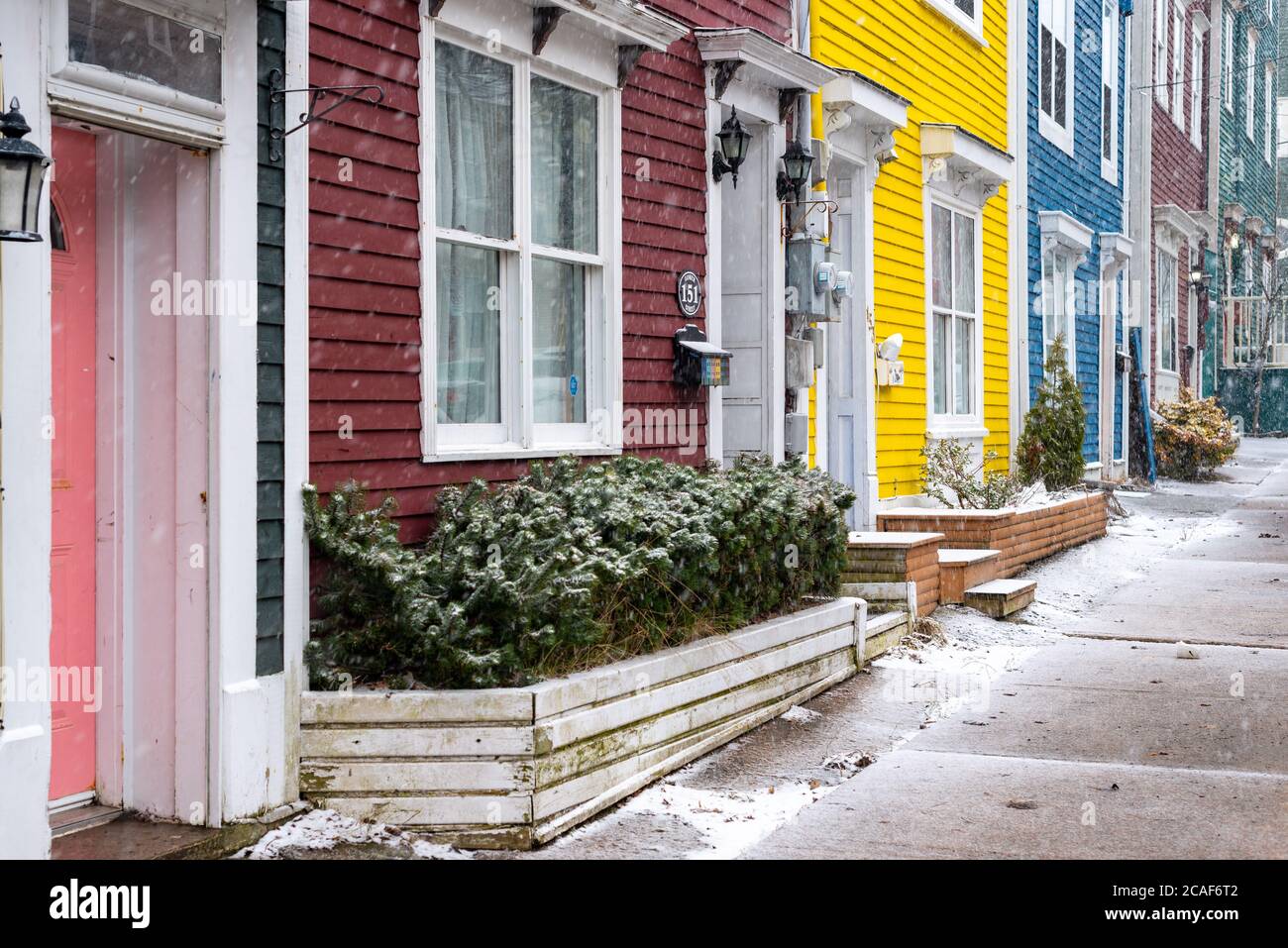Exterior of multiple brightly colorful adjoining row houses with large windows and doors. There's snow on the ground and sidewalk near the buildings. Stock Photo
