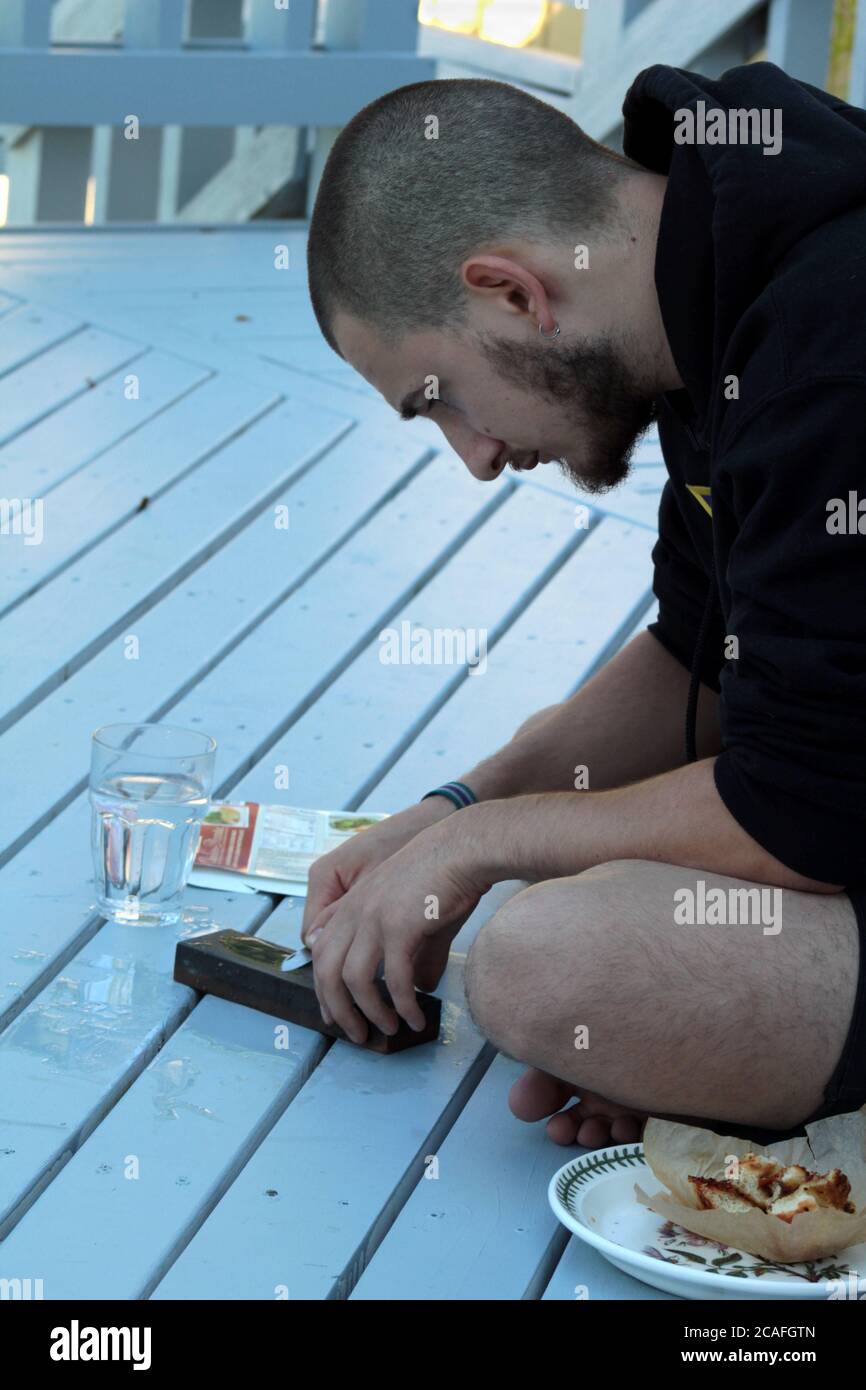 Young man sharpening a knife using a whetstone while sitting in a wood