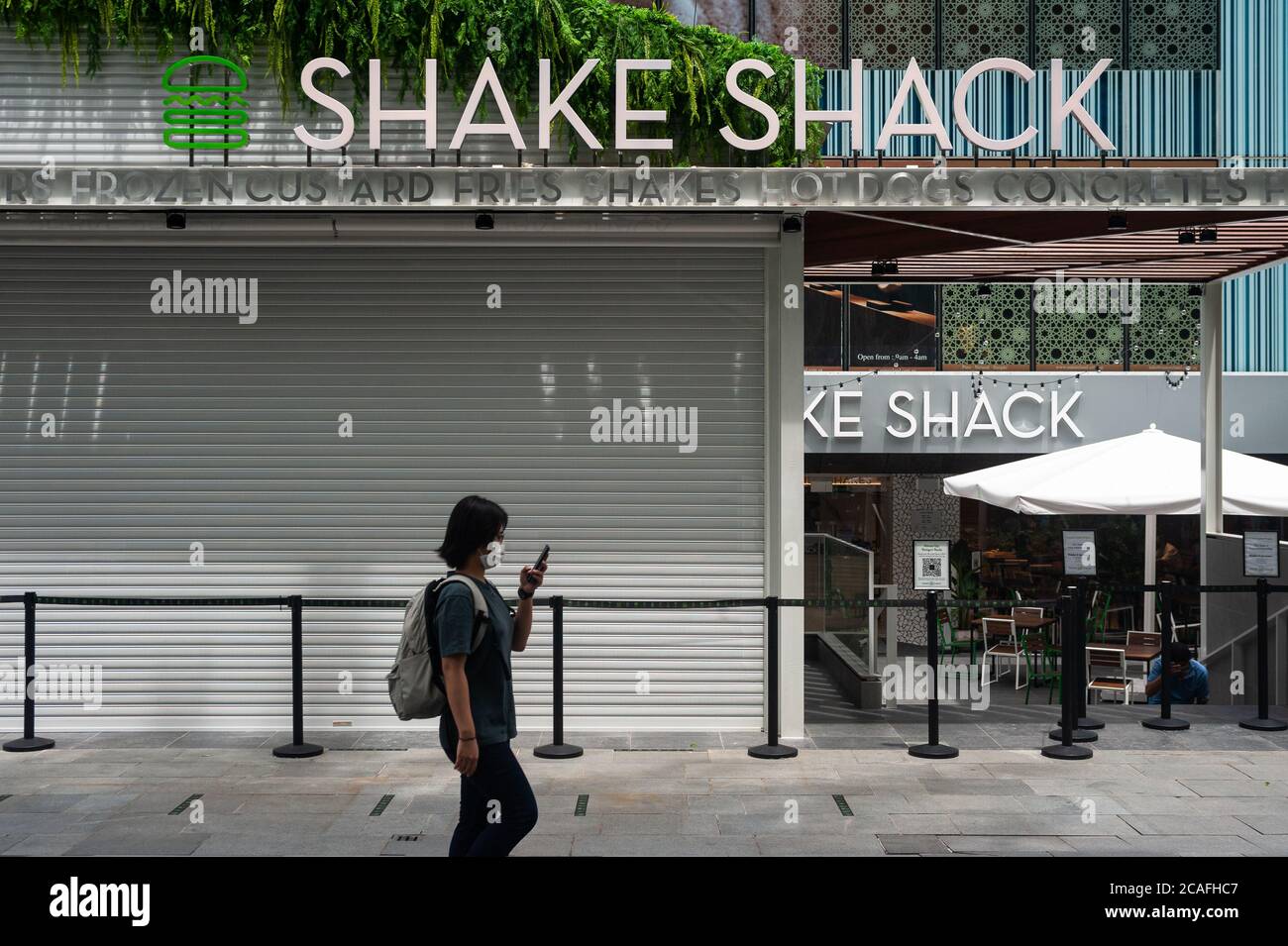 05.08.2020, Singapore, Republic of Singapore, Asia - Woman with face mask to protect against Covid-19 (coronavirus) walks past new Shake Shack outlet. Stock Photo