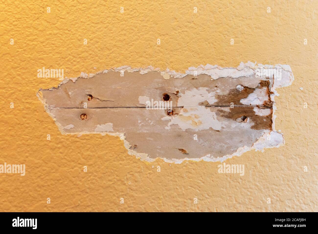 Drywall joint crack repair in progress. Excavated damaged area. Exposed drywall seam with rusty nails. Stock Photo