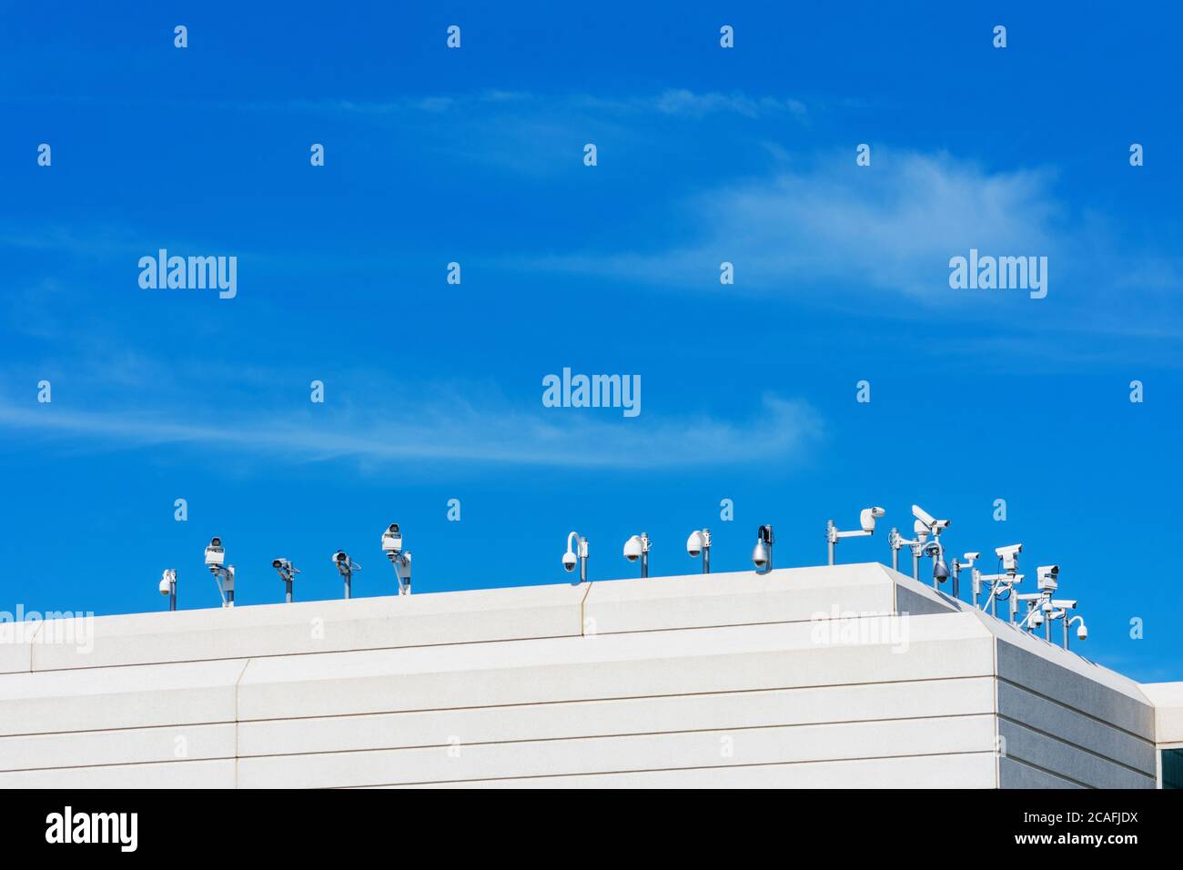 Various outside security cameras cover multiple angles from the rooftop of modern office building under blue sky Stock Photo