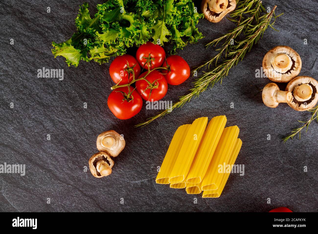 Organic durum wheat pasta with fresh tomato and mushrooms on dark background. Stock Photo