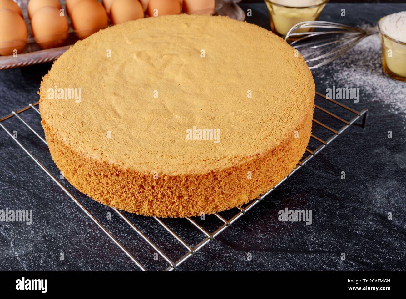 Homemade round sponge cake on gray table with eggs. Stock Photo