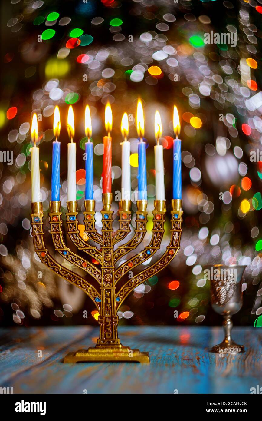 Hanukkah background with menorah and burning candles on sparkle background with defocused colored lights. Stock Photo