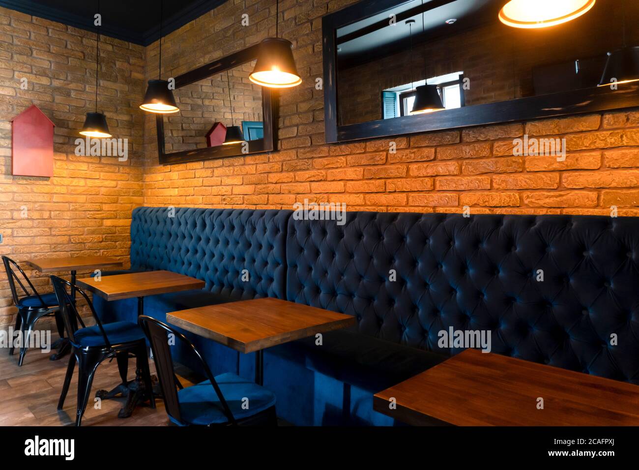 Small dining tables at restaurant, modern loft design, brick wall behind, lamps. Stock Photo