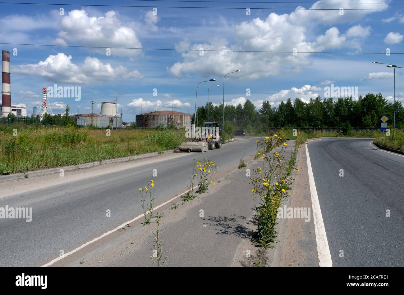 Summer landscape with a tractor on the highway shoveling garbage against the background of thermal power plant and yellow flowers Stock Photo