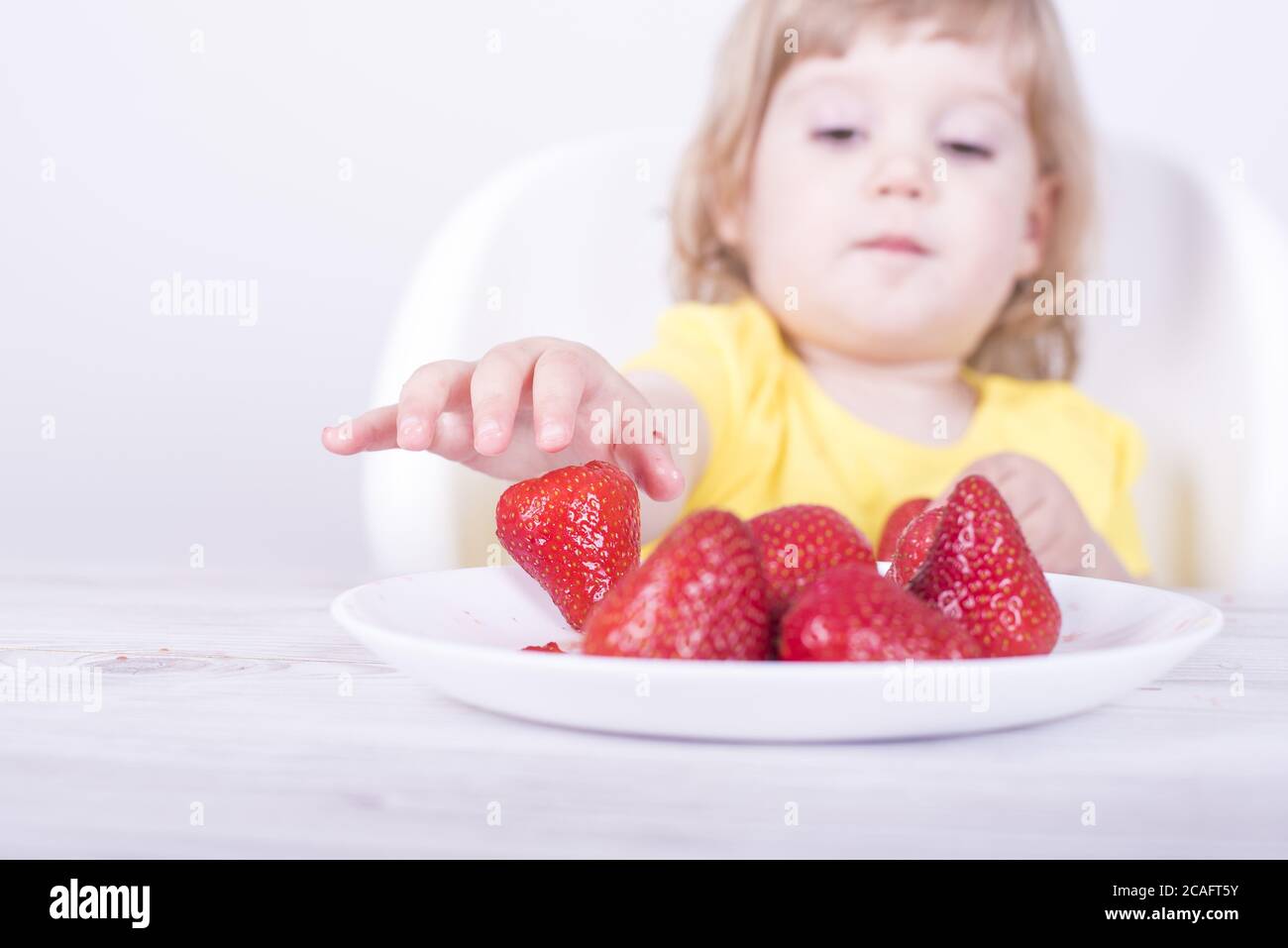 Selective focus shot of a happy little girl eating juicy strawberries Stock Photo