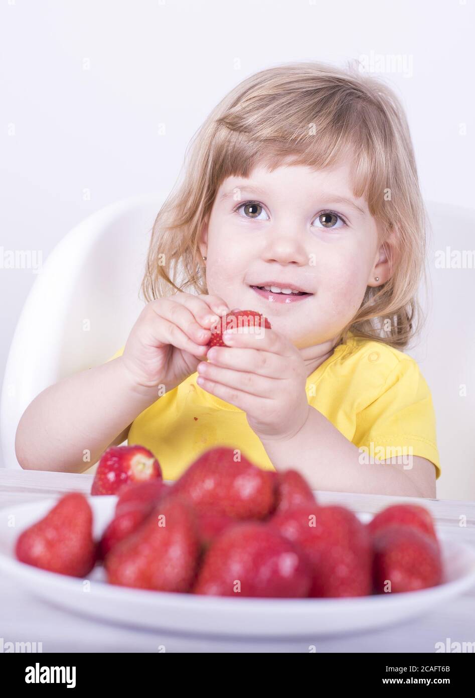 Selective focus shot of a happy little girl eating juicy strawberries Stock Photo