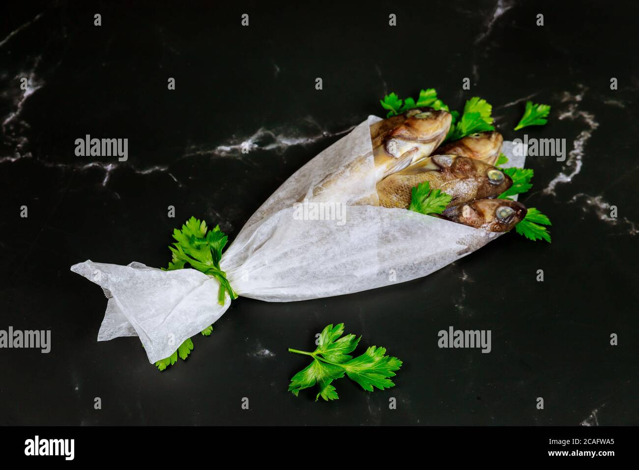 Fresh whole fish with parsley wrapped in parchment paper on black table