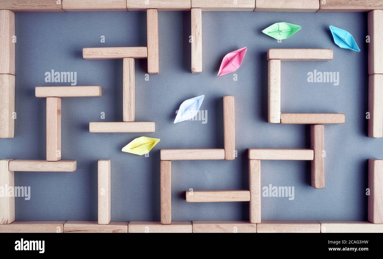 Leadership, guidance or teamwork, concept. Colorful paper boats in line are moving towards the exit in a maze or labyrinth made with wooden blocks. Stock Photo