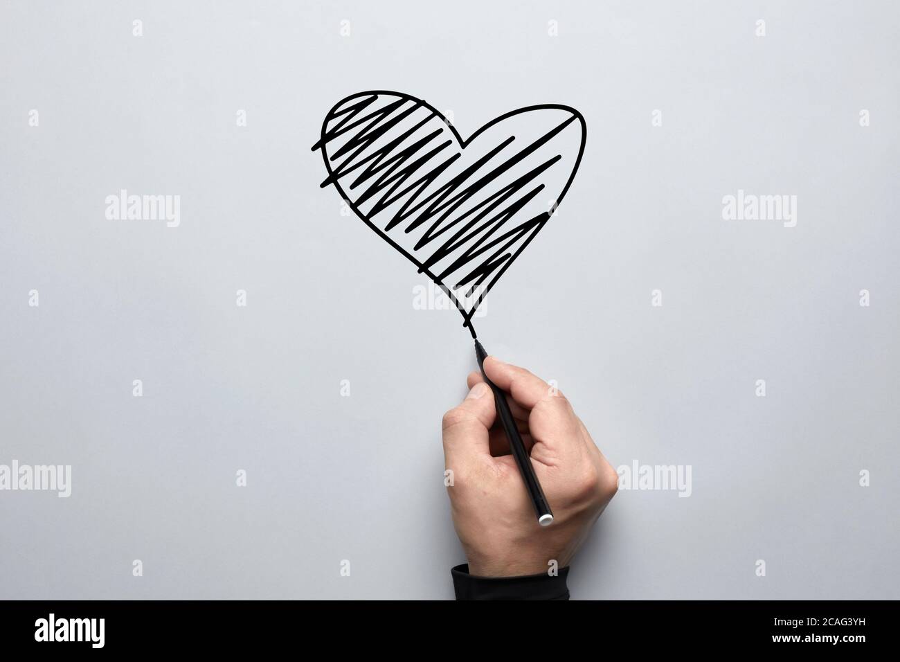 Male hand drawing a heart shape with a black pen on gray background ...
